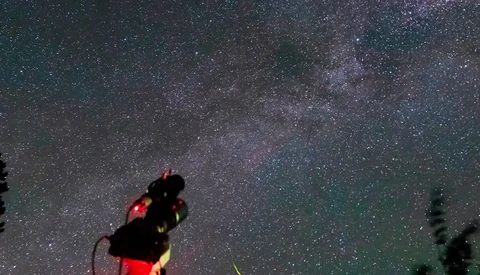 Telescope pointed at night sky filled with stars and Milky Way with red light attachment.