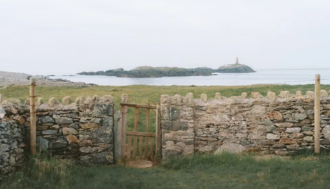 Weathered stone wall with wooden gate overlooking coastal landscape with distant island.