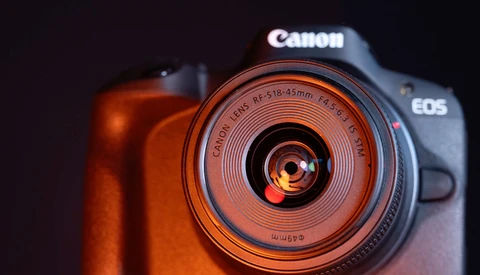 Canon EOS camera with RF 24-105mm lens illuminated by warm orange studio lighting against a dark background.