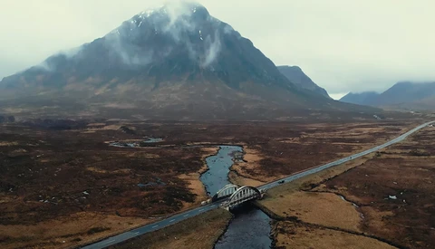 Aerial view of a mountain with a road and river crossing a barren landscape.