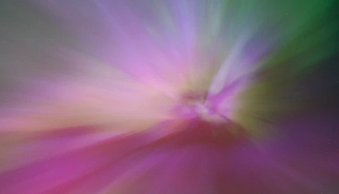 Abstract radial blur with magenta, green, and purple light rays converging toward center.