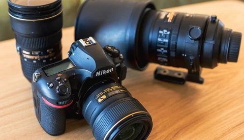 Nikon DSLR camera with attached lens surrounded by additional lenses on wooden surface.