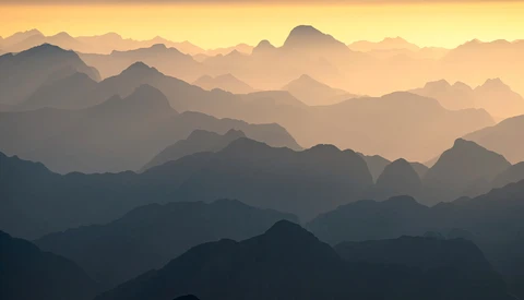 Layered mountain silhouettes fading into atmospheric haze at sunrise or sunset.