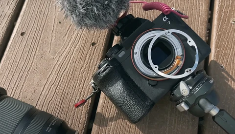 Mirrorless camera with lens removed, showing mount adapter and internal mechanics on wooden surface.