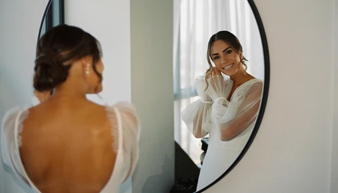 Woman in white shirt viewed from behind looking at her reflection in a round mirror.