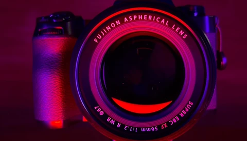 Vintage camera with neon pink and blue lighting against dark purple background.