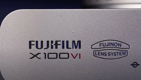 Close-up of Fujifilm X100VI camera body showing branding and Fujinon lens system marking.