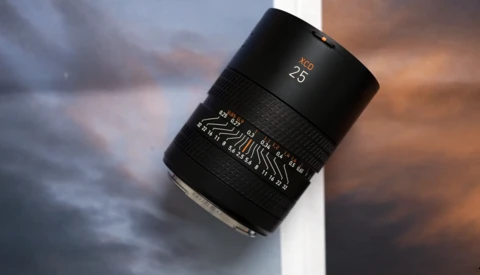 Black telephoto lens with focal length markings displayed against a dramatic cloudy sky backdrop.