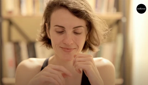 Woman with short blonde hair smiling with eyes closed, hand near face in contemplative pose.