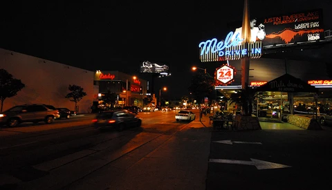 Neon-lit street at night with illuminated signs and storefronts along a commercial strip.