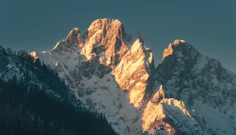 Snow-covered mountain peaks illuminated by golden sunrise light against a deep blue sky.