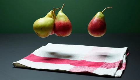 Three pears arranged above a striped kitchen towel against a dark green background.