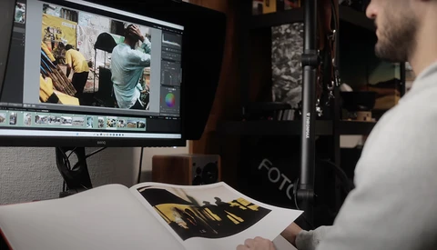 Photographer reviewing edited images on monitor while holding color-corrected print.