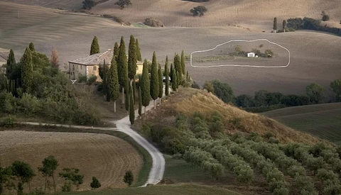Aerial view of a Tuscan villa with cypress trees lining a winding driveway through rolling hills.