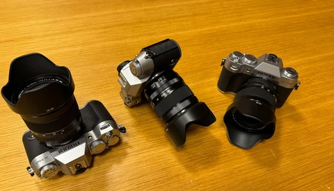 Three vintage rangefinder cameras with attached lenses displayed on a wooden surface.