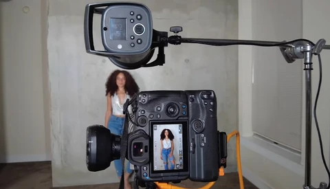 Behind-the-scenes view of a portrait photography setup with a large-format camera displaying a live image of a woman on its LCD screen.
