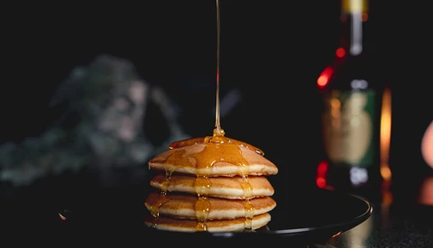 Stack of golden pancakes with syrup being drizzled over the top.