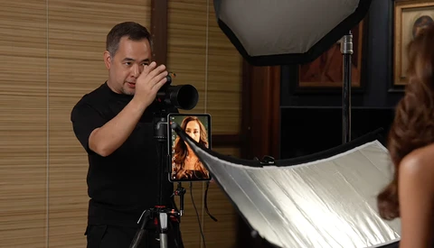Photographer with camera on tripod positioning a reflector during a portrait lighting setup.