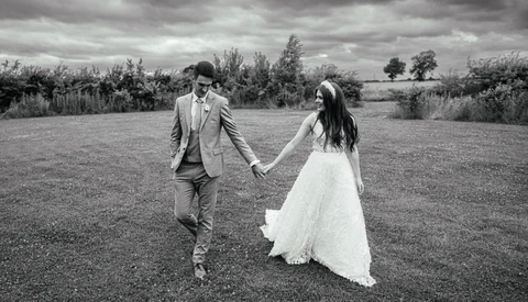 Bride and groom holding hands while walking through an open field in black and white.