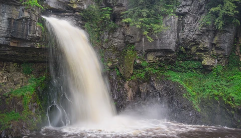 Waterfall cascading down layered rock formations surrounded by lush green moss and vegetation.