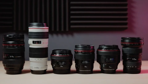 Six camera lenses arranged in a line, displaying varying focal lengths and designs against a pink and dark background.