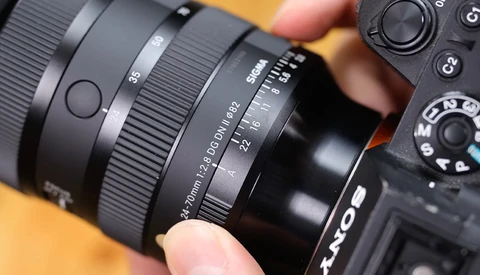 Close-up of a camera lens and camera body being held, showing focus ring and aperture markings.