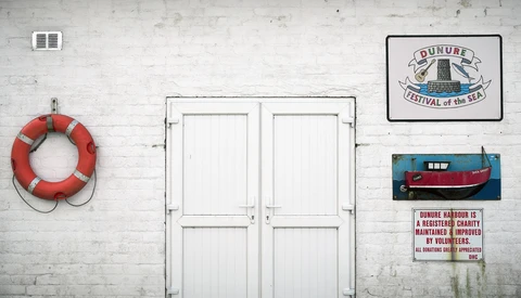 White double doors on weathered wall with life preserver, festival sign, boat painting, and charity plaque.