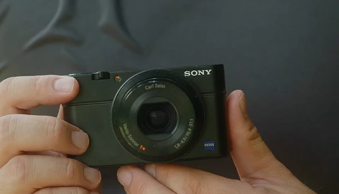 Hands holding a Sony compact camera with Zeiss lens and blue accent detail.