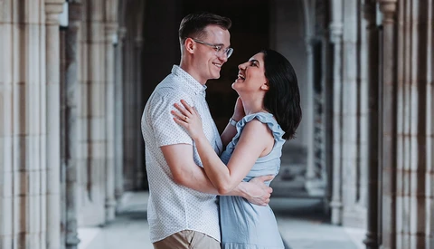 Couple smiling at each other in a columned hallway with soft natural light.