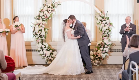 Bride and groom kiss at the altar beneath a floral arch during wedding ceremony.