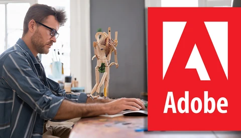 Designer working at desk with wooden mannequin and Adobe logo displayed.