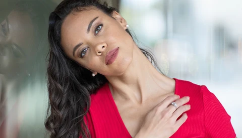 Woman in red top tilting head against blurred urban background.