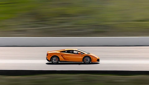 Orange sports car in profile against blurred green and gray background.