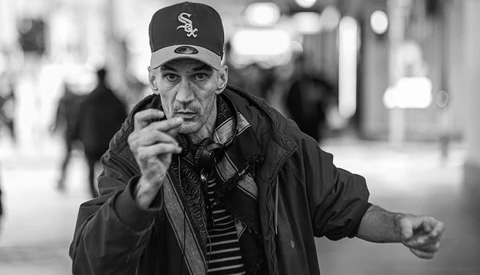 Man in Chicago White Sox cap pointing directly at camera on urban street.