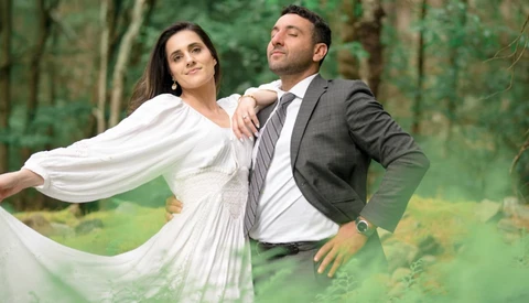 Bride and groom posing together in a forest setting with flowing white fabric.