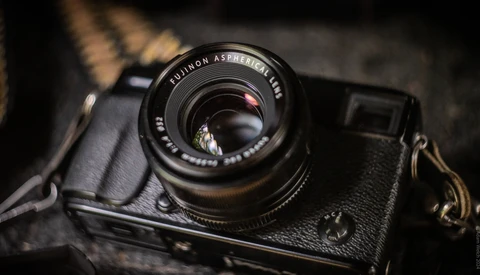 Vintage rangefinder camera with Fujinon lens mounted on dark leather strap against textured background.