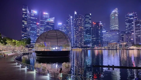 Modern dome structure on waterfront promenade with downtown city skyline reflected in calm water at night.