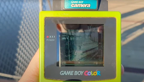 Game Boy Color camera accessory with bright yellow frame displaying interior hallway scene on screen.