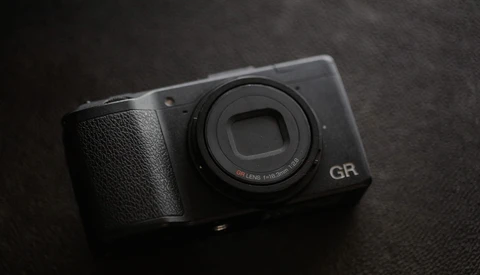 Ricoh GR compact camera with fixed lens on dark textured surface.