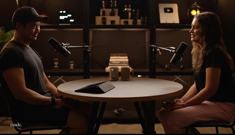 Two people sitting at a round table with microphones in a podcast studio setup.
