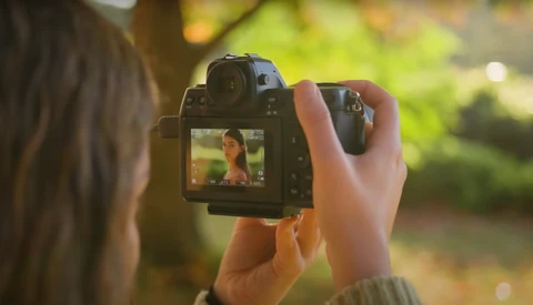 Photographer holding DSLR camera with subject visible on rear LCD screen during outdoor shoot.