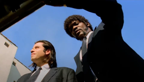 Two men in dark suits photographed from below against a clear blue sky.