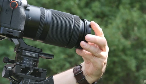 Photographer's hand gripping a telephoto zoom lens mounted on a camera with a tripod head visible below.