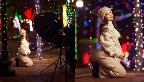 Woman in white fur coat kneeling among colorful holiday lights during a studio photo shoot.