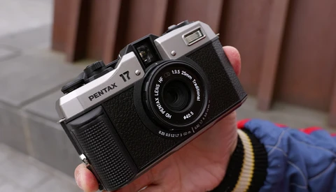 Pentax 17 film camera held in hand, showing chrome top plate and black body with textured grip.