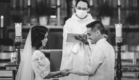 Bride and groom exchange rings at altar while priest holds ceremonial book during church wedding ceremony.