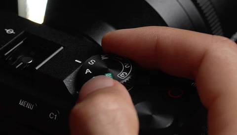 Photographer's hand adjusting the mode dial on a professional camera body.