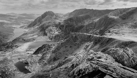Mountain lakes nestled in a rocky alpine valley with winding road visible on distant ridge.