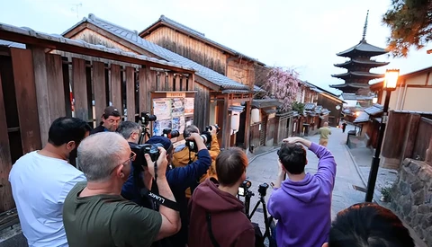 Group of photographers with cameras photographing a traditional Japanese street lined with wooden buildings and a pagoda in the background.