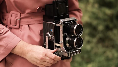 Person in rose-colored jacket holding a twin-lens reflex camera with dual objectives and viewfinder.